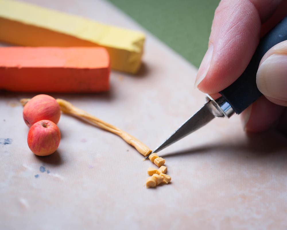 cutting small pieces of apple filling A thin strip of clay being cut into small pieces with a craft knife