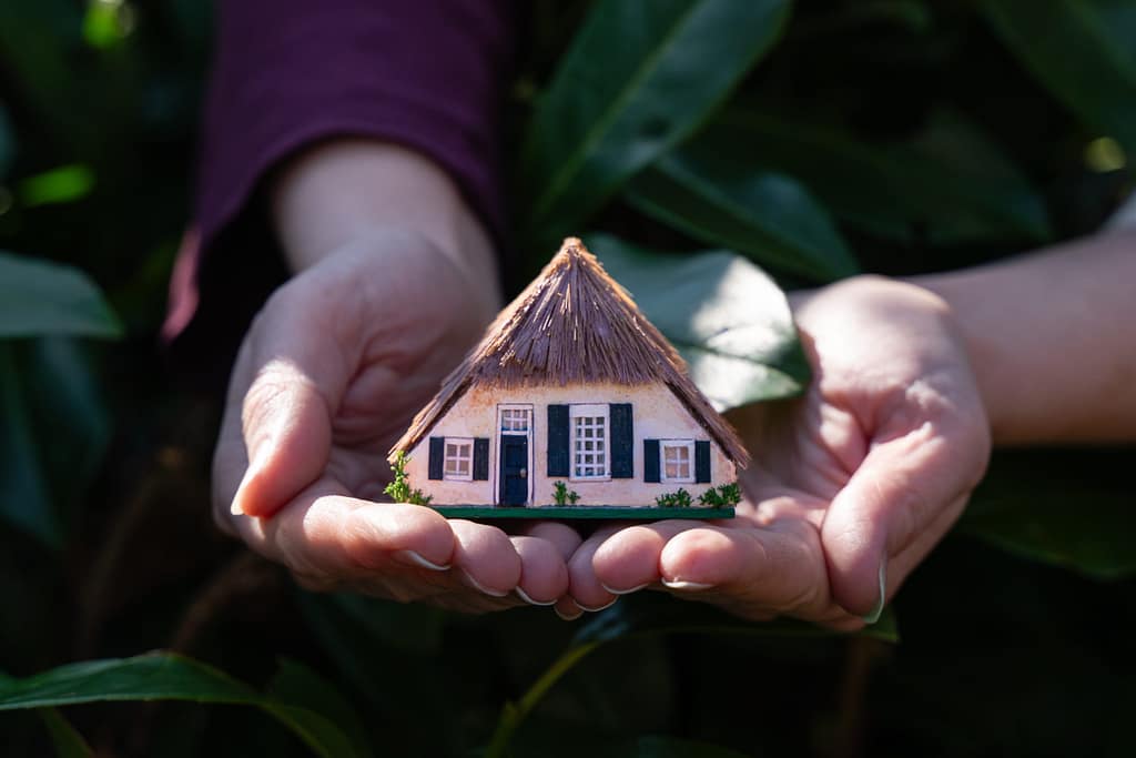 Two hands holding a 1/144 miniature dollhouse made in a farm house style