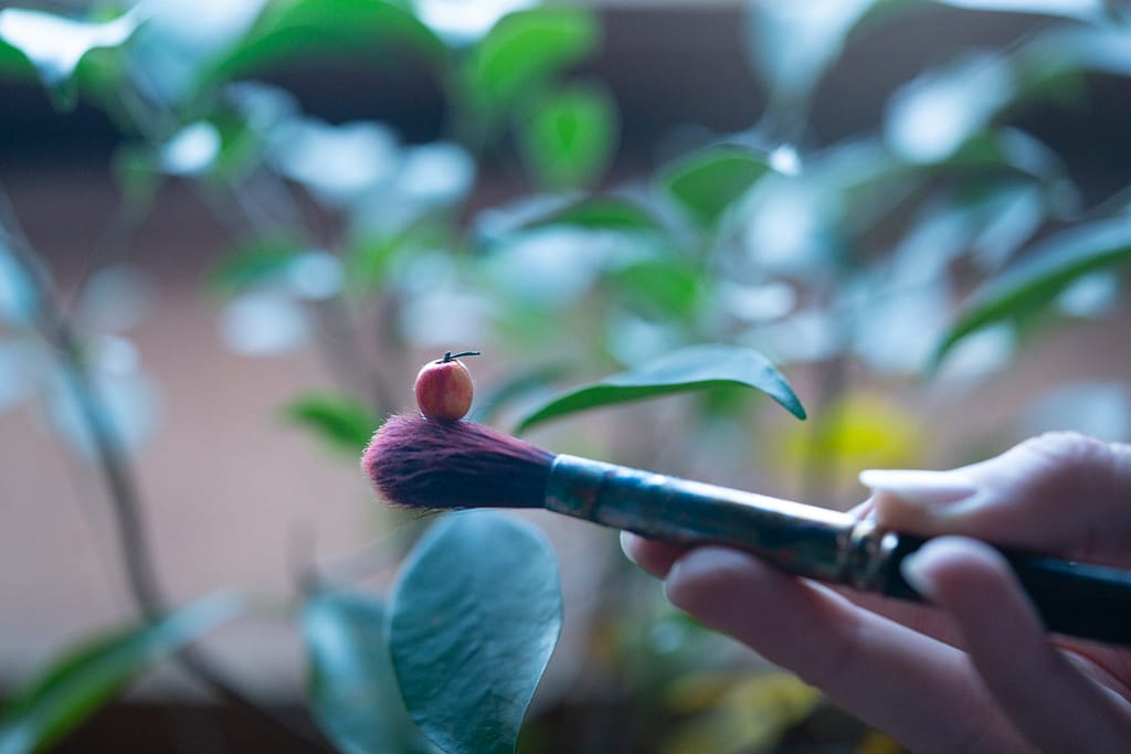 Paintbrush held horizontally with a miniature apple placed on it