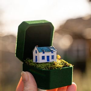 hand holding ring box with Irish cottage A micro miniature white Irish cottage in a green velvet ring box held by a hand